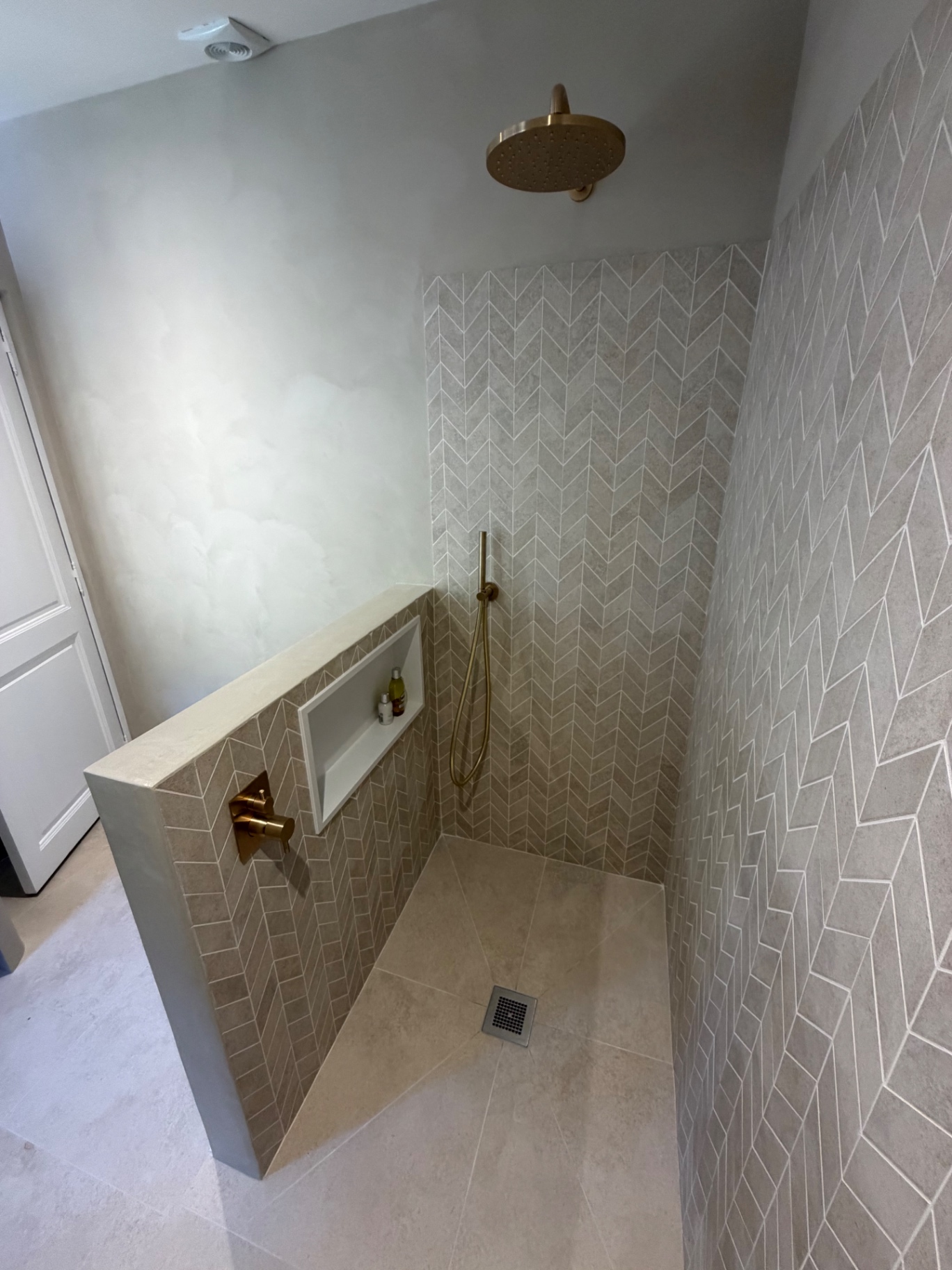 Rénovation salle de bain haut de gamme à Fréjus : douche à l'italienne en carrelage chevron grand format avec robinetterie laiton brossé et niche sur-mesure